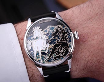May include: A silver wristwatch with a black leather band. The watch face features a detailed design of two horses, one white and one black, set against a mountain backdrop. The watch is a part of the Travel Collection.