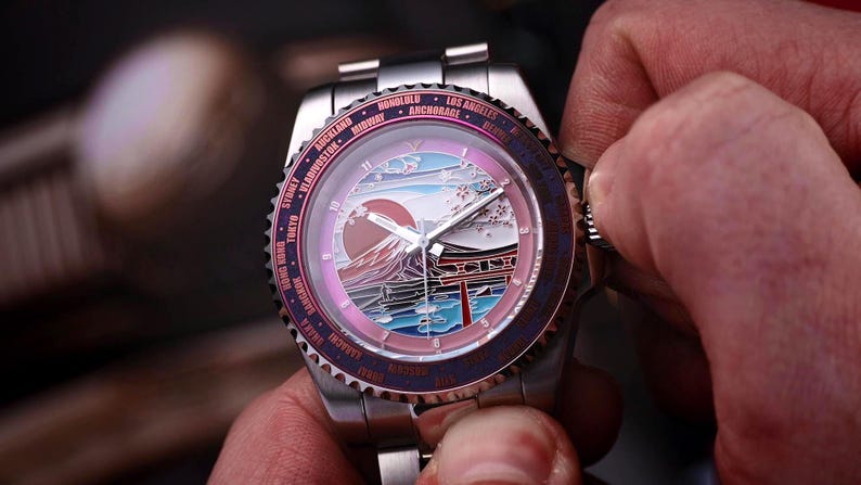 May include: A stainless steel wristwatch with a detailed dial featuring a Japanese landscape with Mount Fuji and a red sun. The watch has a rotating bezel with city names and is being adjusted by a person.