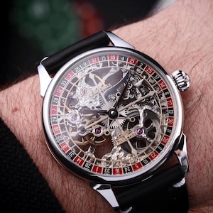 Puede incluir: Un reloj esqueleto plateado con una correa de cuero negro. La esfera del reloj presenta un diseño de ruleta con números rojos y negros. Los intrincados mecanismos internos del reloj son visibles.