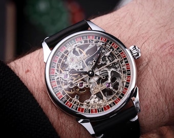 Könnte beinhalten: Eine silberfarbene Skelettuhr mit schwarzem Lederarmband. Das Zifferblatt der Uhr zeigt ein Roulette-Rad-Design mit roten und schwarzen Zahlen. Die komplizierten Innenmechanismen der Uhr sind sichtbar.