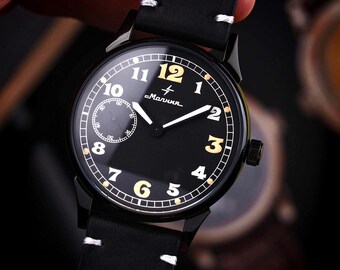 May include: A black wristwatch with a black leather band. The watch face is black with gold-colored numerals and hands. A smaller dial is located at the 9 o'clock position. The watch has the word "Malnn" printed on the face.