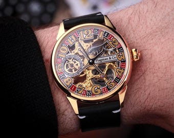 May include: Gold-toned wristwatch with a black leather band. The watch face features a skeleton design with visible gears, gold numerals, and the text "Flagman & Co.". The watch is on a wrist.