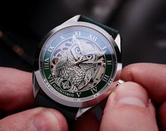 May include: A silver wristwatch with a green face and a black leather band. The watch face features a detailed owl design and Roman numerals. The brand name "FLAGMAN&CO" is visible on the watch face.