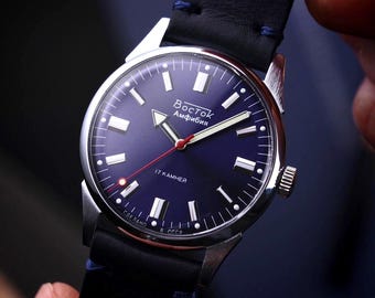 Könnte beinhalten: Nahaufnahme einer Vostok Amphibia-Uhr mit blauem Zifferblatt, silbernem Gehäuse und schwarzem Lederarmband. Das Zifferblatt hat weiße Markierungen, einen roten Sekundenzeiger und den Text "Восток Amphibia".
