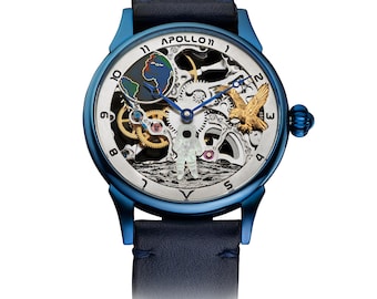 Könnte beinhalten: Blaue Armbanduhr mit Skelettzifferblatt mit einem Astronauten, einem goldenen Adler und einer Darstellung der Erde. Die Uhr hat ein blaues Lederarmband und den Text "APOLLO 11" oben.