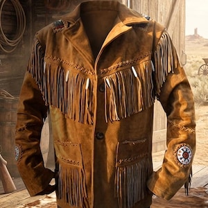 Puede incluir: Chaqueta de ante marrón con flecos en el pecho, las mangas y la espalda. La chaqueta tiene parches decorativos en los hombros y las mangas, y una parte delantera abotonada. La chaqueta se muestra frente a una puerta de madera y un paisaje del oeste.