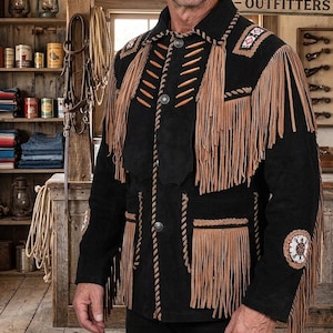 Könnte beinhalten: Schwarze Wildlederjacke mit beigefarbenen Fransen und dekorativen Perlen. Die Jacke hat einen Reverskragen, Knopfverschlüsse und Taschen mit Fransen. Ein Kleidungsstück im Western-Stil.