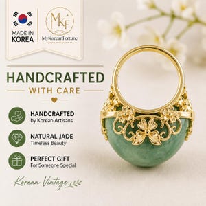 Op de afbeelding: Een gouden ring met een gladde, ronde basis van groene jade, versierd met gedetailleerd goudkleurig bloemfiligraan. De tekst op de afbeelding bevat "MADE IN KOREA", "MyKoreanFortune", "HANDCRAFTED WITH CARE" en "Korean Vintage".