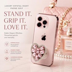 May include: A light pink smartphone with a heart-shaped phone grip featuring pink crystals and a silver border. The text reads: LUXURY CRYSTAL HEART PHONE GRIP, STAND IT. GRIP IT. LOVE IT. Stable. Elegant. Effortless. STRONG HOLD, STURDY STAND, LUXURIOUS DESIGN.