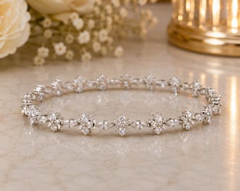 May include: A silver-toned bangle bracelet featuring a repeating pattern of marquise and round-cut clear stones. The circular jewelry piece is constructed with alternating floral-like clusters and elongated stone settings in a continuous design.