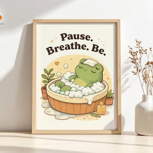 Peut inclure: Une affiche encadrée représentant une grenouille de dessin animé se relaxant dans une baignoire en bois remplie de bulles. Le texte "Pause. Breathe. Be." est écrit en marron. Une petite bougie et des plantes en pot sont également représentées.