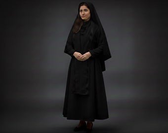 May include: A full-length image of a person wearing a black garment, including a long dress and a head covering. The outfit has long sleeves and a modest neckline. The person is standing against a dark gray background.