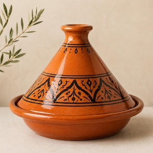 Può includere: Pentola tagine in ceramica arancione con coperchio conico e base ampia e poco profonda. Il coperchio presenta motivi decorativi neri e una piccola apertura. Utensile da cucina tradizionale.