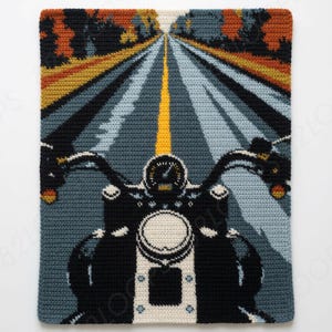 May include: A rectangular crochet tapestry featuring a first-person perspective of a motorcycle riding down a road. The scene includes a black motorcycle dashboard, handlebars, and a headlight, with a yellow center line and autumn trees.