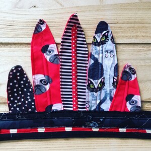 May include: A red, black, and white fabric headband with a variety of patterns, including stars, stripes, polka dots, and animal prints. The headband features a pug and cat design.