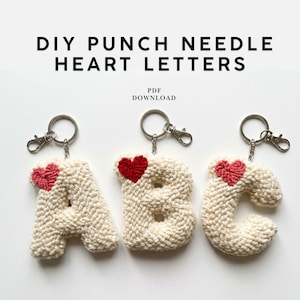 May include: Three handmade keychains featuring the letters A, B, and C, each crafted from off-white yarn and adorned with a red heart. The keychains have silver-colored clasps and rings. The text "DIY PUNCH NEEDLE HEART LETTERS" is at the top.