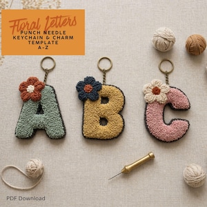 Op de afbeelding: Drie sleutelhangers in de vorm van de letters A, B en C, elk versierd met een bloemenontwerp. De letters zijn groen, geel en roze, met donkergrijze randen. De afbeelding bevat ook bollen garen en een punch needle tool.