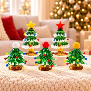 May include: A collection of five miniature glass Christmas trees in various designs. Two trees feature white snow-like trim and star toppers, while three smaller trees are adorned with colourful glass bulbs and solid sphere toppers.