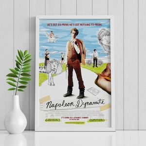 May include: Framed movie poster for "Napoleon Dynamite" with a white border. The poster features a central figure in a brown suit, surrounded by sketched characters and the film's title. Text includes "HE'S OUT TO PROVE HE'S GOT NOTHING TO PROVE."