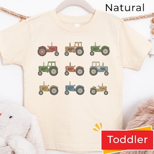 May include: A natural-colored short-sleeve t-shirt featuring a grid of nine illustrated tractors in various colors including red, orange, green, blue, and yellow. The graphic print is centered on the front of the shirt, which has a crew neckline.