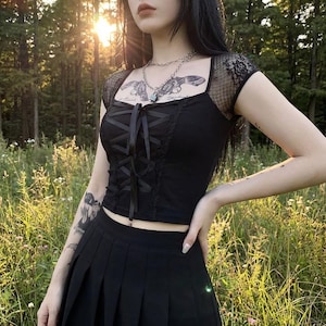 Top corto gótico: top gótico con corsé negro y mangas de encaje, estilo urbano alternativo y oscuro.