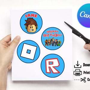 May include: A sheet of paper with four circular designs featuring Roblox characters and logos. One design says "Jake", another says "Happy Birthday", and the others feature the Roblox logo. The image also includes the Canva logo and instructions to download, print, and cut.