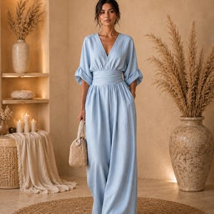 May include: A light blue jumpsuit featuring a deep V-neckline, wide three-quarter length sleeves with gathered cuffs, and a wide cinched waistband. The garment has a relaxed, floor-length silhouette with wide legs and a textured fabric finish.
