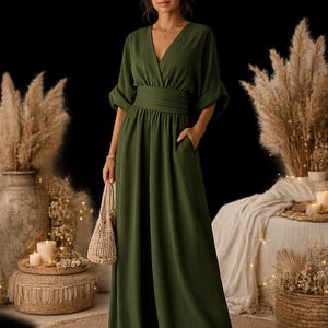 May include: An olive green jumpsuit featuring a deep V-neckline, three-quarter length sleeves with cuffed hems, a wide pleated waistband, and wide-leg trousers with side pockets. The garment is solid-coloured and has a floor-length hemline.