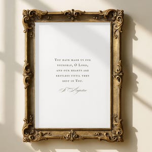 May include: A framed print with a gold ornate frame. The print features the quote "YOU HAVE MADE US FOR YOURSELF, O LORD, AND OUR HEARTS ARE RESTLESS UNTIL THEY REST IN YOU." in black text on a white background.