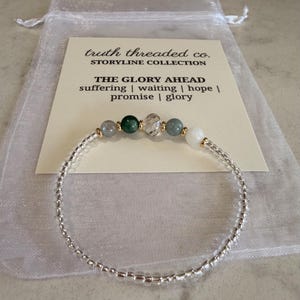 May include: A beaded bracelet with a mix of colorful gemstones and silver beads. The bracelet is displayed on a card with the text "truth threaded co. STORYLINE COLLECTION THE GLORY AHEAD suffering | waiting | hope | promise | glory". The bracelet is in a white organza bag.
