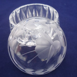 May include: A clear glass trinket box with a frosted floral design on the lid. The box has a round shape and a fluted base.