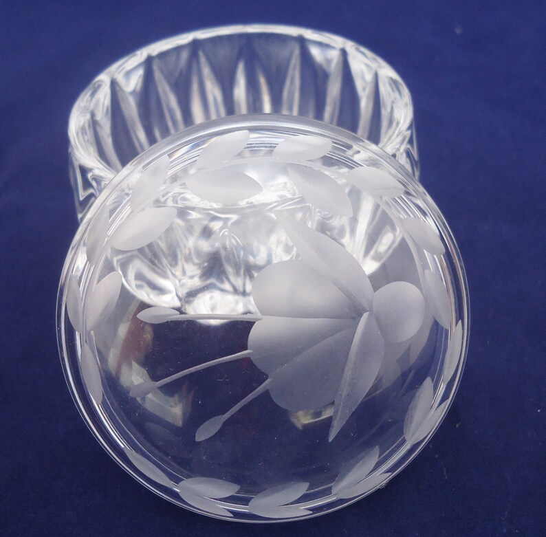 May include: A clear glass trinket box with a frosted floral design on the lid. The box has a round shape and a fluted base.