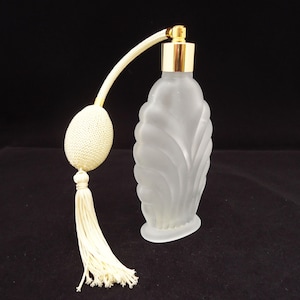 May include: A frosted glass perfume bottle with a vertical scalloped pattern, featuring a gold-tone metal collar and a cream-coloured fabric atomizer bulb with a matching tassel attached by a flexible tube to the top of the bottle.