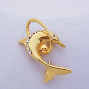 May include: A gold-toned dolphin brooch with clear rhinestones. The dolphin is curled in a circle and has a tail that extends to the side.