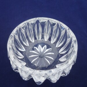 May include: A clear glass bowl with a scalloped edge and a starburst pattern on the bottom. The bowl is made of crystal and has a delicate, elegant design.