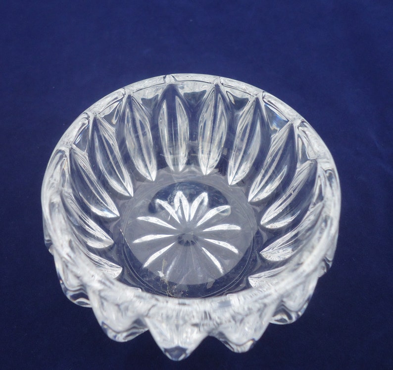 May include: A clear glass bowl with a scalloped edge and a starburst pattern on the bottom. The bowl is made of crystal and has a delicate, elegant design.