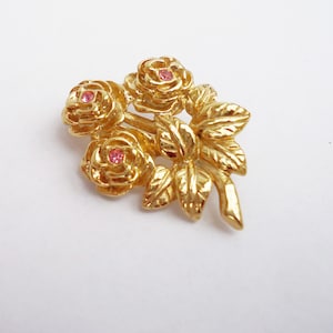 May include: Gold-toned brooch featuring three roses with pink rhinestone centers and detailed leaves.