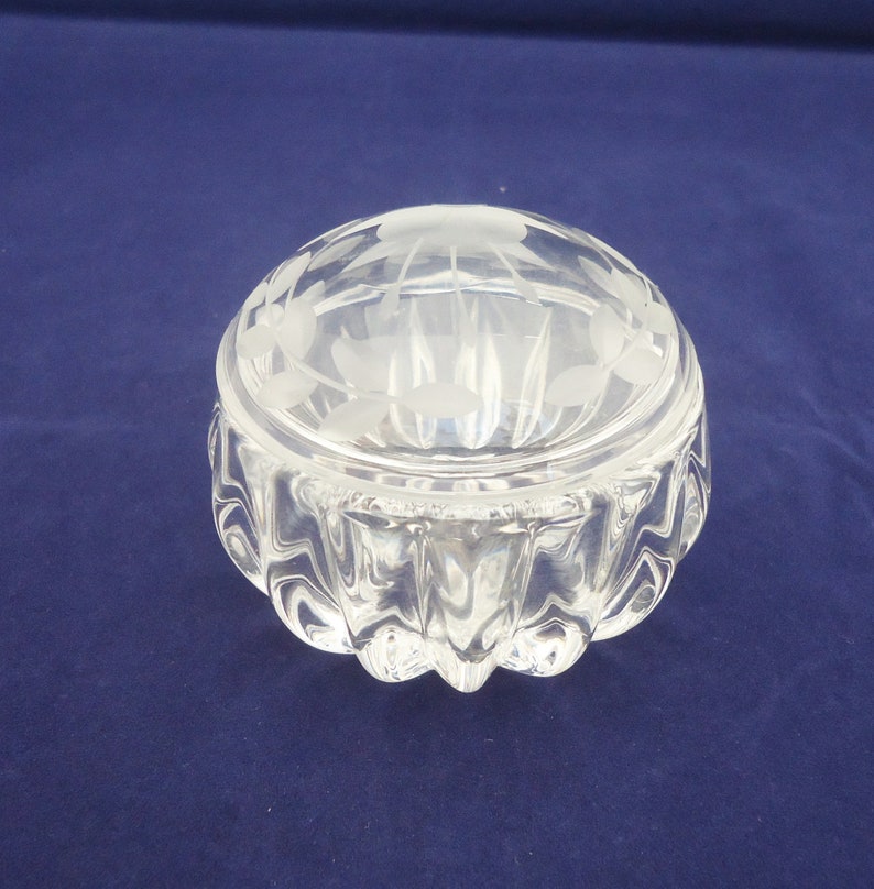 May include: A clear glass trinket box with a frosted floral design on the lid. The box has a rounded base with a textured design.