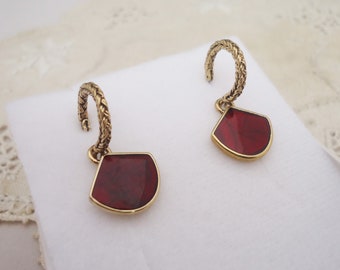 May include: A pair of gold hoop earrings with a red, geometric pendant. The hoops are braided and the pendants are shaped like a fan.
