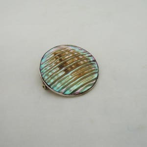 May include: A round, iridescent abalone shell brooch with a silver setting. The shell has a swirling pattern of light and dark green, brown, and gold.