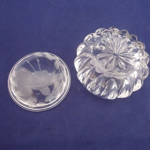 May include: A clear glass bowl with a frosted floral design on the lid. The bowl has a scalloped edge and a starburst pattern on the bottom.