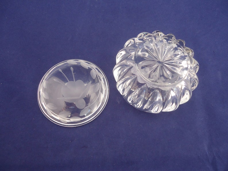 May include: A clear glass bowl with a frosted floral design on the lid. The bowl has a scalloped edge and a starburst pattern on the bottom.