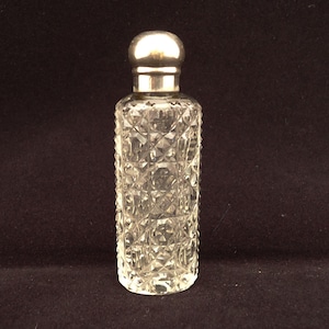 May include: A clear glass perfume bottle featuring a cylindrical body with a deep, multifaceted diamond-cut pattern. The bottle is topped with a smooth, rounded, metallic silver-toned cap that sits securely on the narrow neck of the vessel.