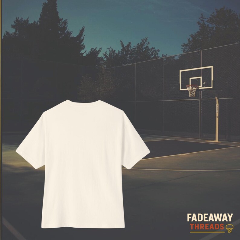 May include: Cream-colored short-sleeved t-shirt with a basketball court in the background. The shirt is the primary focus, with a basketball hoop and trees visible. The brand name "Fadeaway Threads" is in the lower right corner.