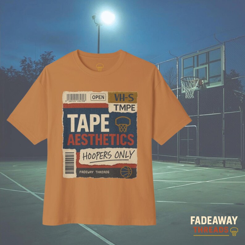 May include: Mustard-colored t-shirt with a graphic design featuring the words "TAPE AESTHETICS HOOPERS ONLY" in a vintage style. The design includes a basketball hoop and a barcode. The shirt is displayed on a basketball court.