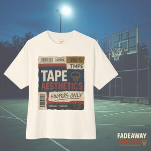 May include: Off-white t-shirt with a graphic design featuring the words "TAPE AESTHETICS HOOPERS ONLY" in a vintage style. The design includes a basketball hoop and a barcode. The shirt is set against a basketball court background.
