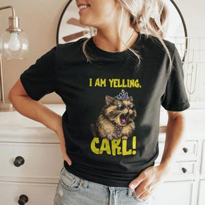 May include: Black t-shirt with a graphic of a cat wearing sunglasses and a crown, with the text "I AM YELLING, CARL!". The cat is brown and tan with its mouth open. The text is yellow.