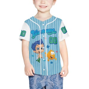 May include: A light blue baseball jersey with white sleeves and a v-neck collar. The jersey features the text "Your name" and the number "00" in green and blue. Cartoon characters are printed on the front.