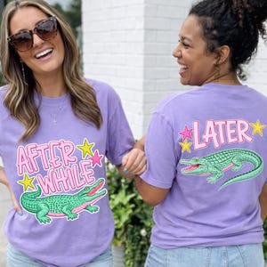 Puede incluir: Dos mujeres con camisetas lavanda con un diseño de cocodrilo de dibujos animados. La parte delantera de la camiseta dice "AFTER A WHILE" con una estrella. La parte trasera de la camiseta dice "LATER" con una estrella y un cocodrilo verde.