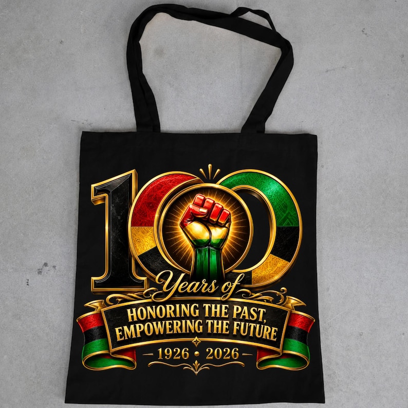 K&ouml;nnte beinhalten: Schwarze Tragetasche mit einem Grafikdesign zum 100-j&auml;hrigen Jubil&auml;um. Das Design umfasst eine geballte Faust, die Zahl 100 und den Text "Years of Honoring the Past, Empowering the Future - 1926-2026". Das Design enth&auml;lt Rot, Gr&uuml;n, Schwarz und Gold.